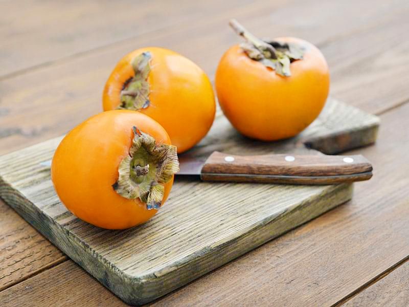 Three persimmons on a wooden board with a knife